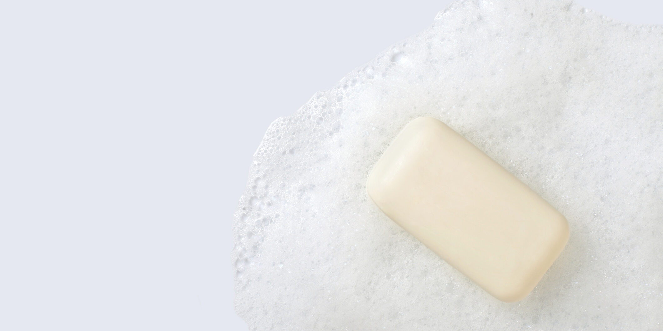 A cream colored bar of soap with soap suds on a white background