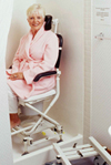 A woman in a pink bathrobe sits in a shower chair