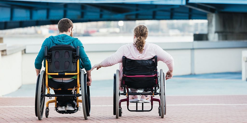 The back of a man and woman in wheelchairs holding hands