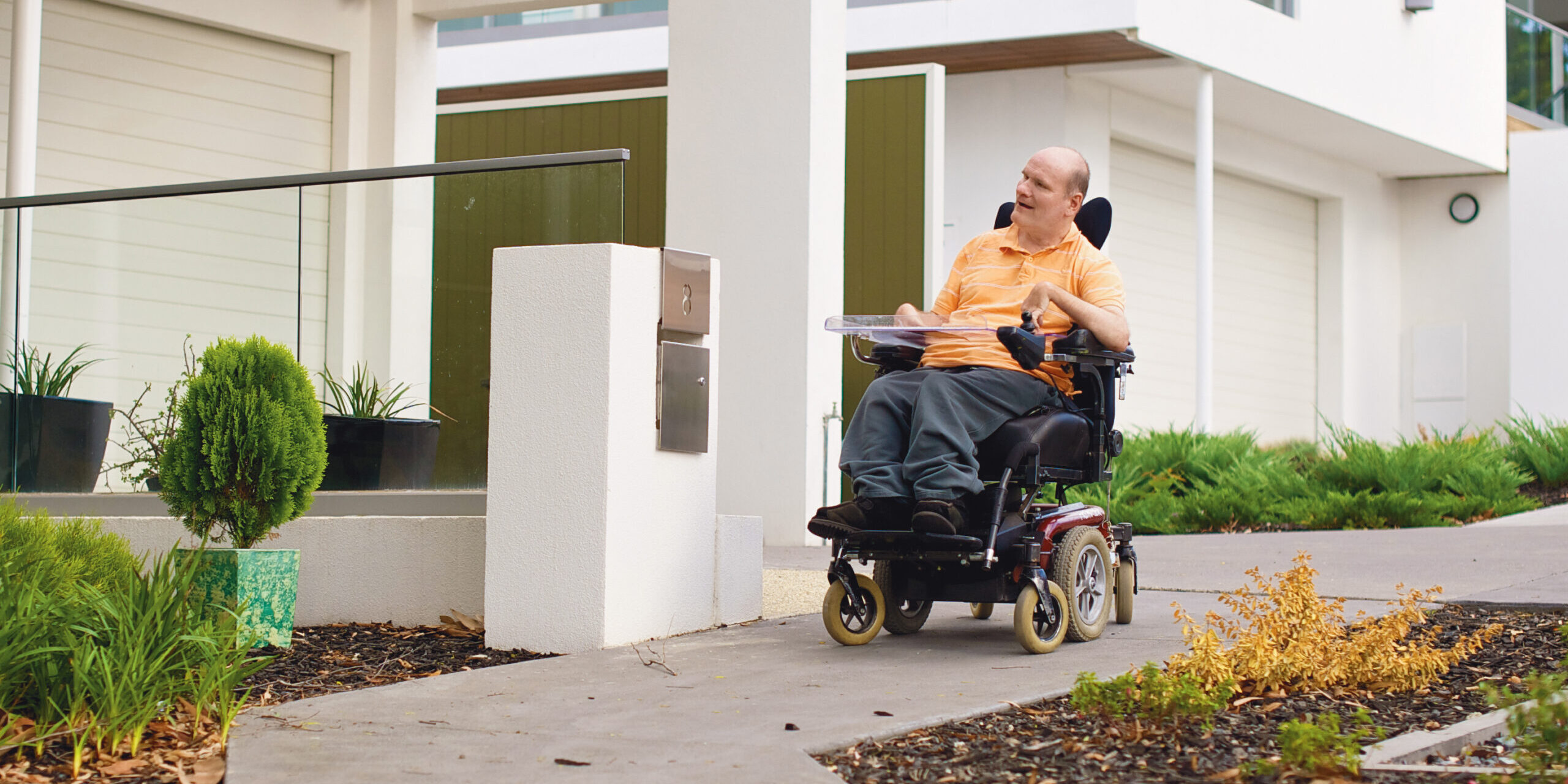 Man in an electric wheelchair on a footpath in a suburban setting.