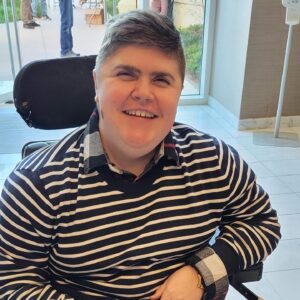 Charlie smiling in a striped shirt and power wheelchair