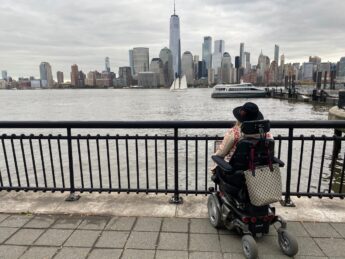 Jax Cowles in power wheelchair with her back to camera as she looks at the New York City skyline.