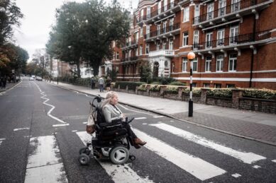 Jax Cowles using a power wheelchair and crossing a city crosswalk in London