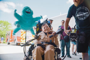 Carter wears a Ghostbusters costume while seated in his Ghostbusters-themed wheelchair, a model of a ghost from the movie looming over his right shoulder.