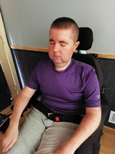 Mark Eisenberg sits in a relaxed position in his power wheelchair, with his hands resting on his knees and his eyes closed. 