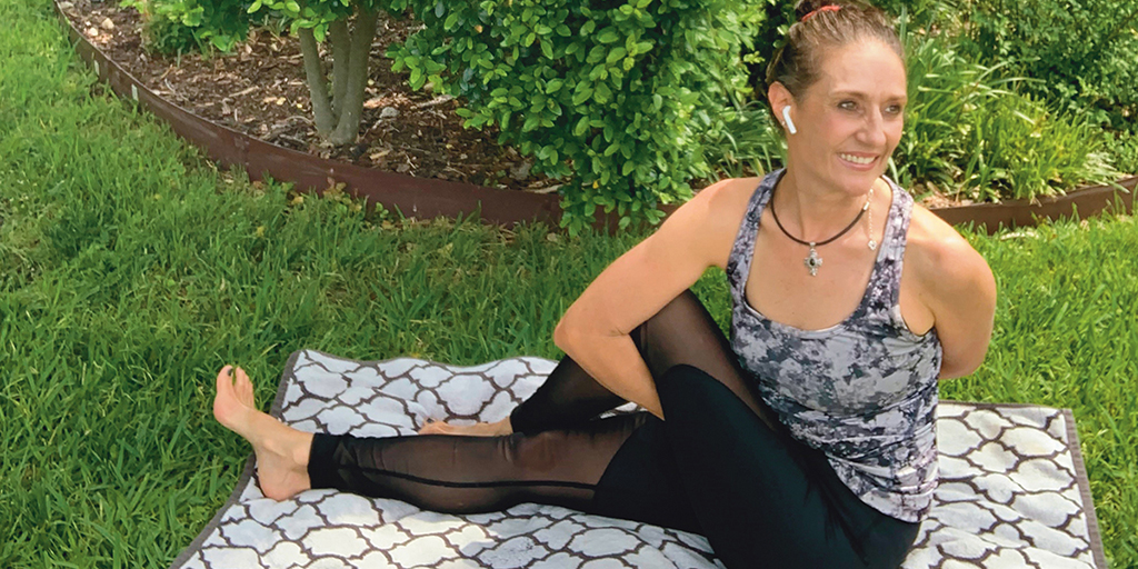 Health and wellness coach Michele MacArthur performs a twisting stretch seated on a blanket spread over the grass.