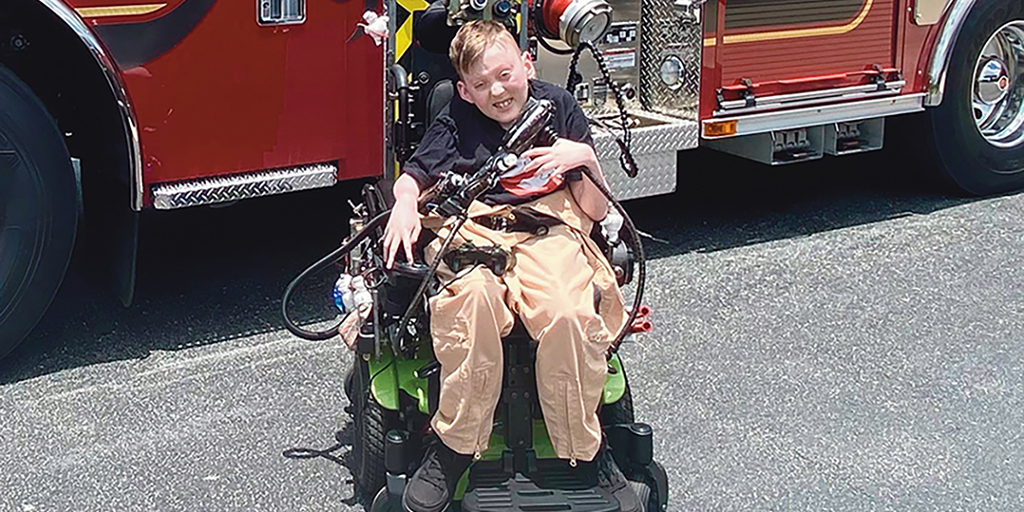 9-year-old Carter Rhodes is positioned in front of a fire truck in his power wheelchair outfitted to look like a gunner seat from the “Ghostbusters: Afterlife” movie.