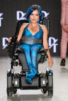 A woman in a haltered blue suit uses a wheelchair on a fashion runway