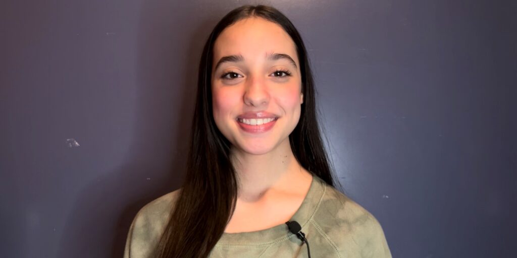 Headshot of a smiling teenage girl with dark straight hair and a microphone clipped to her shirt