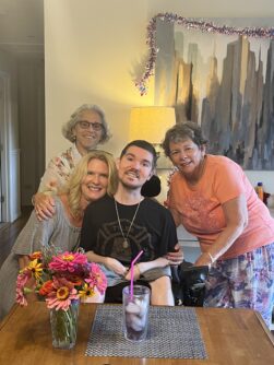 Beckley sits in his wheelchair in the living room of his new home, with his mother, his lawyer, and a friend standing around him.