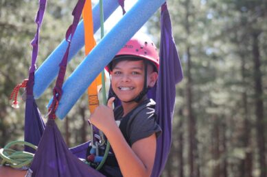 A camper smiles while in a zip line harness.