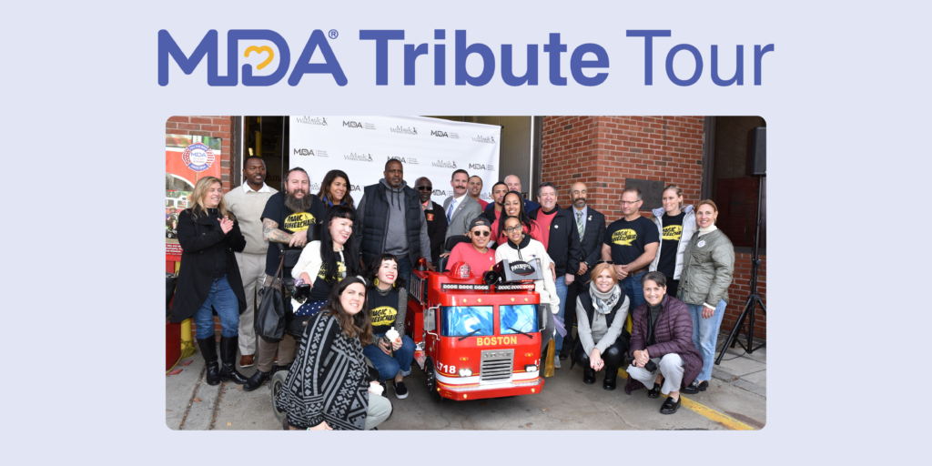 A group of MDA staff, IAFF Firefighters, and Magic Wheelchair staff gather around Jose in his firetruck wheelchair costume.