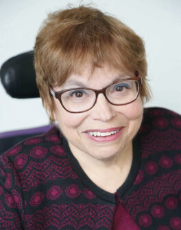 Headshot of Judith Heumann, a white woman with short brown hair and glasses, seated in a power wheelchair.