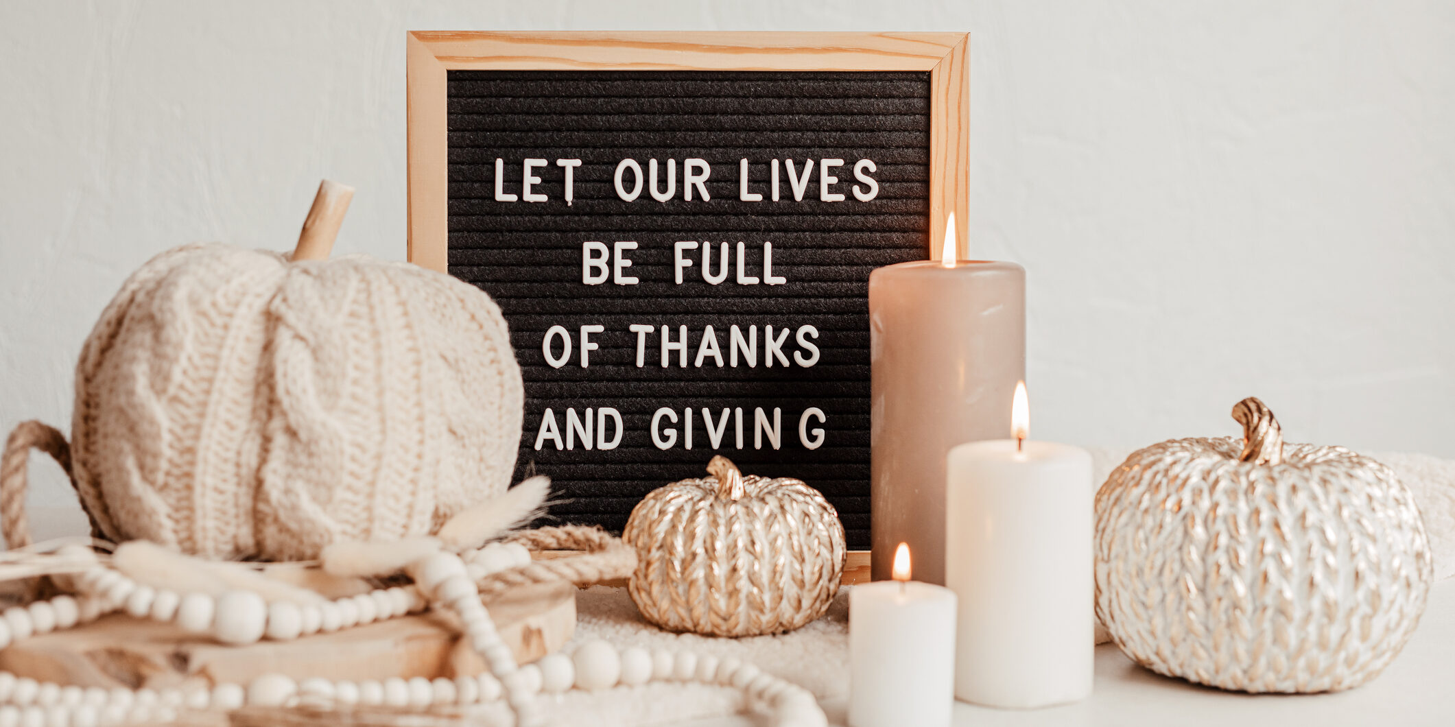Candles and white, crochet pumpkins arranged around a letter board sign that reads: Let our lives be full of thanks and giving