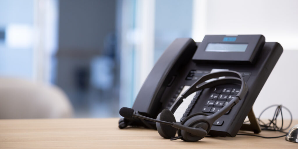 Black landline phone with headset on wooden desk