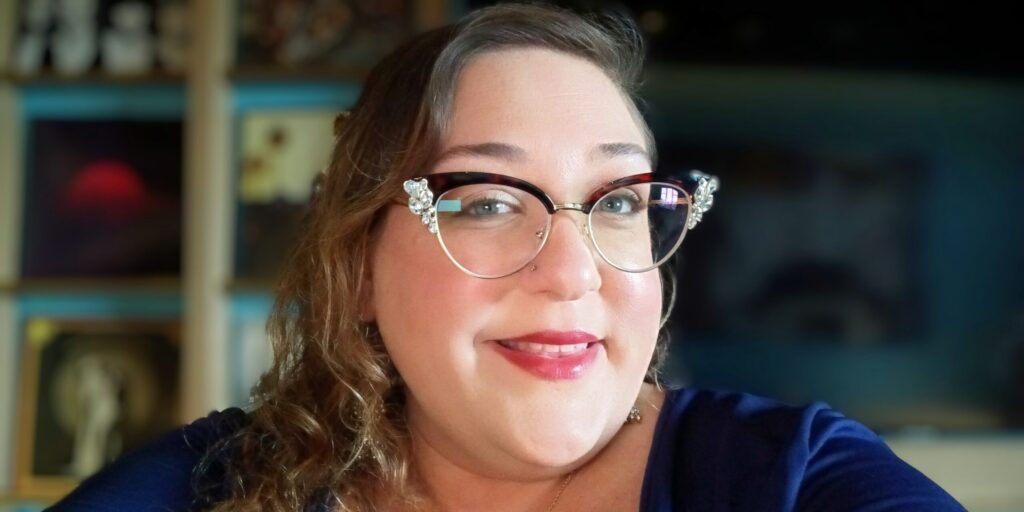 Headshot of Aimee Zehner, a white woman with curly, light brown hair wearing cat-eye, rhinestone-tipped glasses.