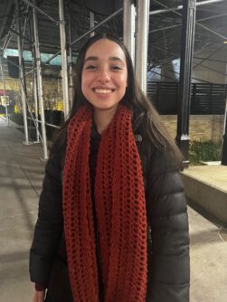 Leah Zelaya, a teenage girl with long brown hair, smiles wearing a black puffy coat and large red scarf