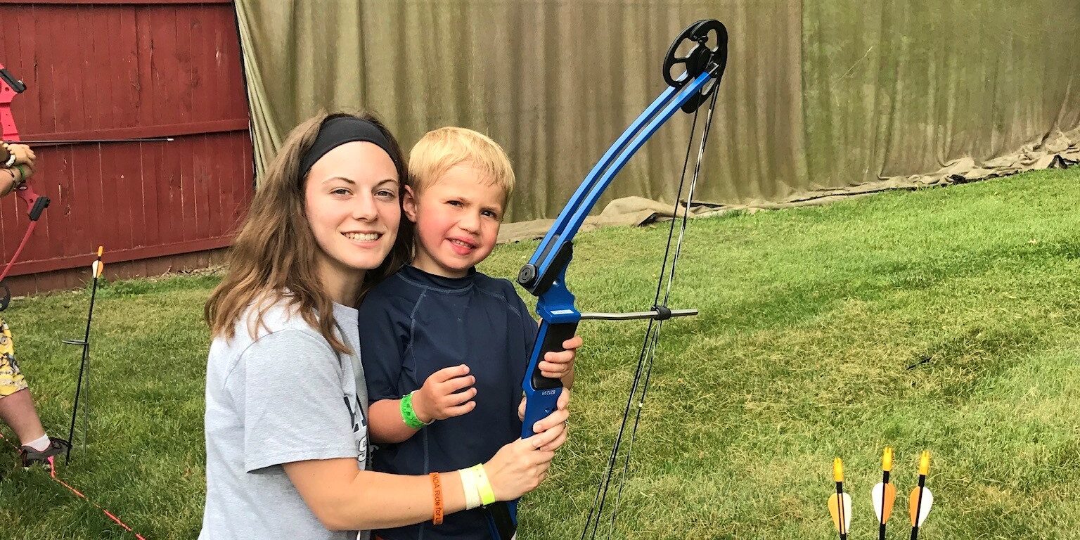 Volunteer camp counselor Hannah Tapia poses with camper Ryan, holding a bow and arrow outside