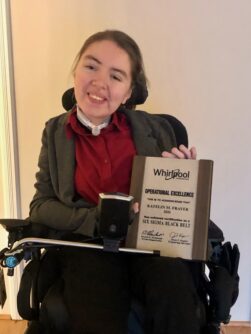 Katie smiles while holding an award of excellence from Whirlpool
