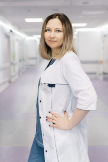 A female doctor in a white lab coat stands with her hand on her hip. 