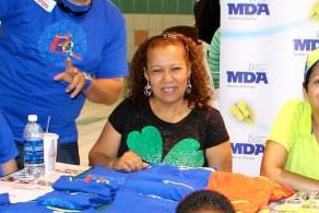 Kathia smiles from a table covered with t-shirts at an MDA event