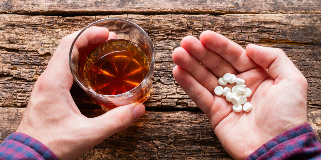 Top view of a man's hands holding a glass of alcohol and a handful of pills