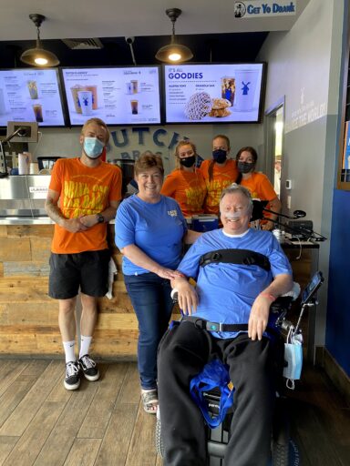 Four staff members wearing masks and two community members, one in a wheelchair, pose inside a Dutch Bros location