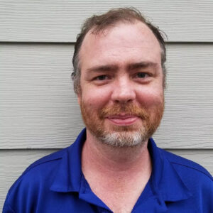 Closeup of Matthew Colvin, a white man with short, reddish-brown hair and beard, wearing a blue shirt.