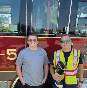 Closeup of Talon Smith and his uncle Kirby Walker standing in front of a fire truck, both wearing sunglasses.