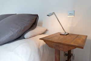 A bedside table with light switches on the wall just above table height and electrical outlets just below.