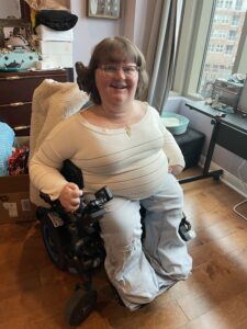 Katrina Kelly, a white woman with short, light brown hair and glasses, sits in a power wheelchair.