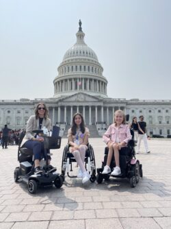Three women in wheelchairs pose in front of the United States Capitol building