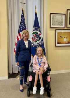 A young woman in a wheelchair poses with a Senator in front of the American flag