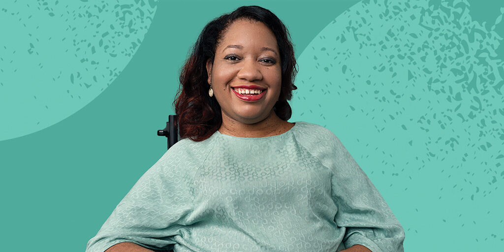 Closeup of Letitia Tatum, a Black woman with curly, shoulder-length, dark brown hair. She is wearing an aqua shirt, sitting in a black wheelchair, against an aqua background.