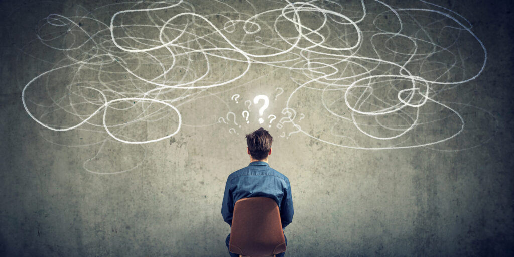 Back view of a thoughtful young businessman sitting on chair looking at a scribble on a wall feeling confused with too many questions