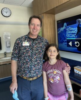 A doctor stands next to a young girl in a patient room