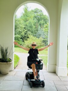 woman dressed in b lack sitting in a scooter with her arms raised 