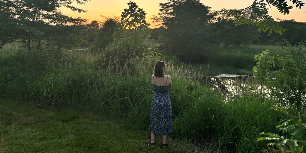 woman in blue dress standing in the grass with her back towards the camera