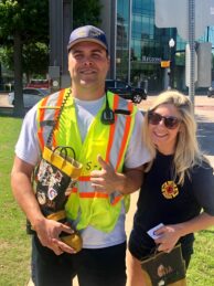 A firefighter in a yellow vest and a woman in a firefighter t-shirt stand side by side outside smiling