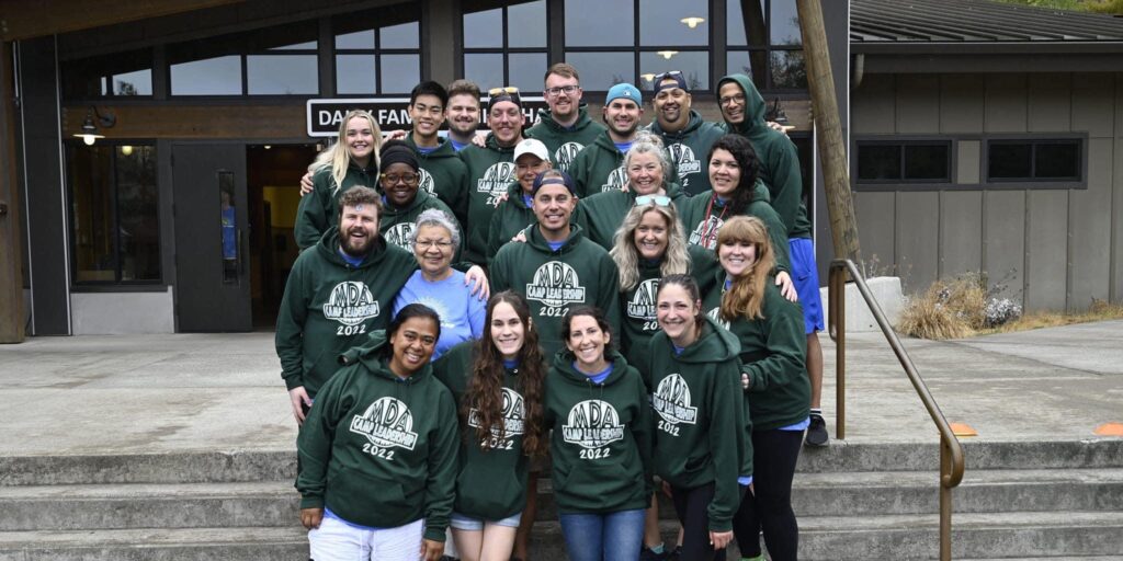 Large group of MDA staff and volunteers wearing matching green sweatshirts stand on a set of outdoor steps