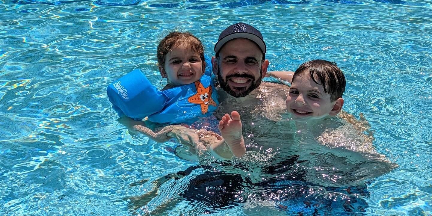 Man floating in pool with two children hugging him