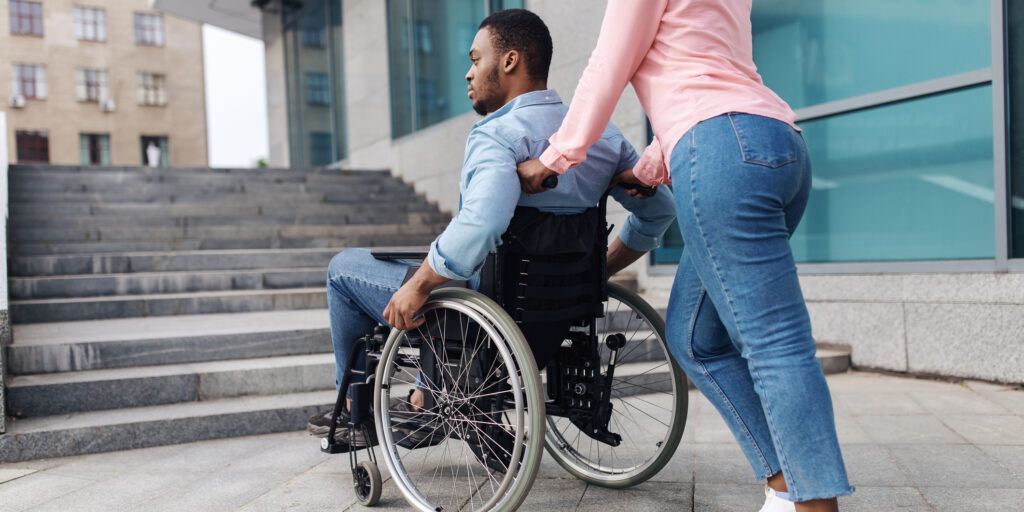 Problems with accessible environment for people with physical disability. Young black woman with millennial man in wheelchair having no possibility to enter building without ramp, outdoors