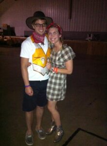 A couple in cowboy and cowgirl costumes smile in a gymnasium