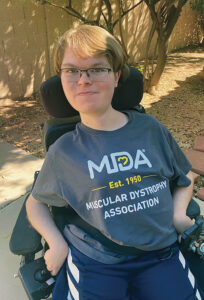 AJ Likhatskaya smiles for the camera in his Muscular Dystrophy Association blue and yellow t-shirt while outside. 