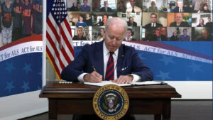 A closeup of U.S. President Joe Biden leaning over his desk and signing a paper with a pen. 