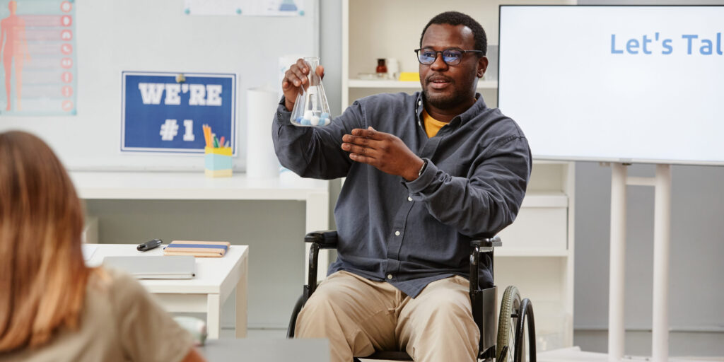 Portrait of African American teacher in wheelchair holding glass beaker during chemistry class in school