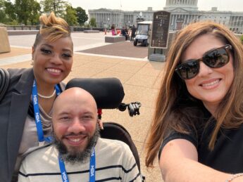 Two woman pose with a man in a wheelchair outside of the U.S. Capitol