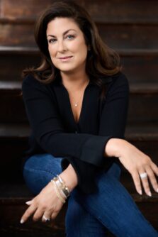 Headshot of a woman with dark brown hair and a black shirt resting her arms on crossed legs