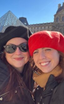 Two woman in berets pose outside of the Louvre in Paris
