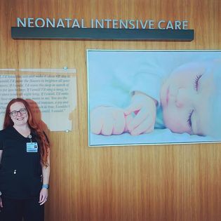 A woman in scrubs stands next to a wall with the words Neonatal Intensive Care inside a hospital 